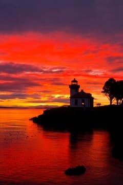 9Sunset-Lime-Kiln-Lighthouse-240x360 | Sea Quest Kayak Tours A lighthouse on a small island during a vibrant sunset, with the sky and water reflecting deep reds and oranges.