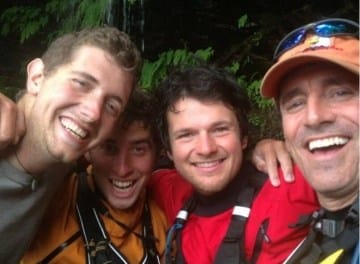 Four smiling people wearing outdoor gear, likely on a kayaking or hiking trip, posing for a close-up photo.
