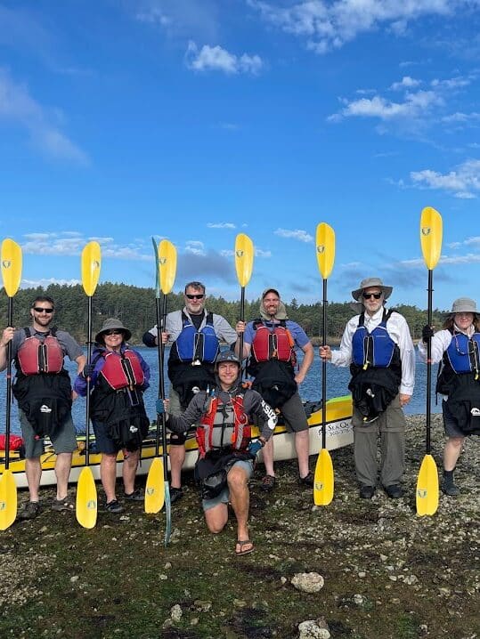 IMG_4158-Kelly-Charlton | Sea Quest Kayak Tours A group of kayakers posing with their paddles on a sunny day.