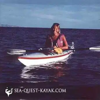 Person sitting in a white kayak on calm water wearing a life jacket and smiling at the camera with the text SEA QUEST KAYAKCOM at the bottom of the image