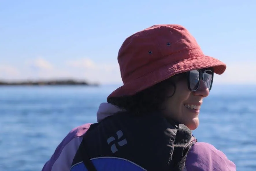 A person wearing sunglasses and a red hat smiling with an ocean backdrop