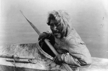 An Inuit man in traditional clothing paddling a kayak.