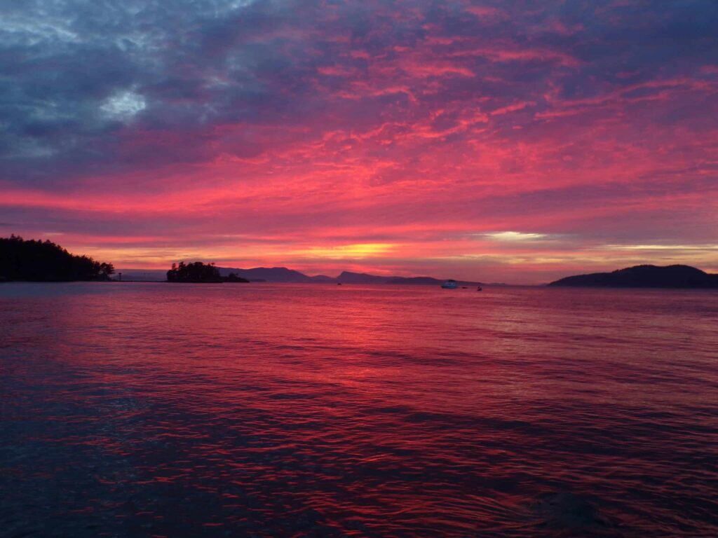 kayak-date-romantic-sunset-1-scaled.jpg | Sea Quest Kayak Tours A stunning sunset over the water with vibrant pink, purple, and orange hues illuminating the sky and reflecting on the calm sea, with silhouettes of islands and a boat in the distance.