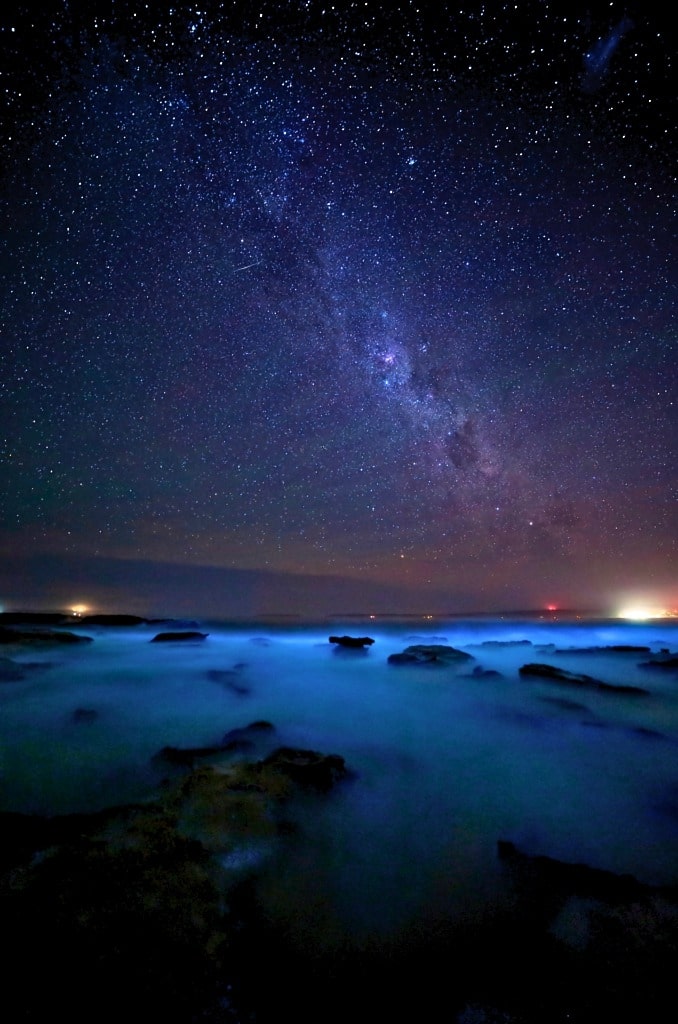 Bioluminescence Kayak Tours in the San Juan Islands: What Makes Them So Special 1 A star-filled night sky with the Milky Way above a rocky shoreline, where glowing blue water hints at bioluminescence—perfect for a magical Bioluminescence-Kayak-Tour beneath the stars. ,Bioluminescence Kayak Tours