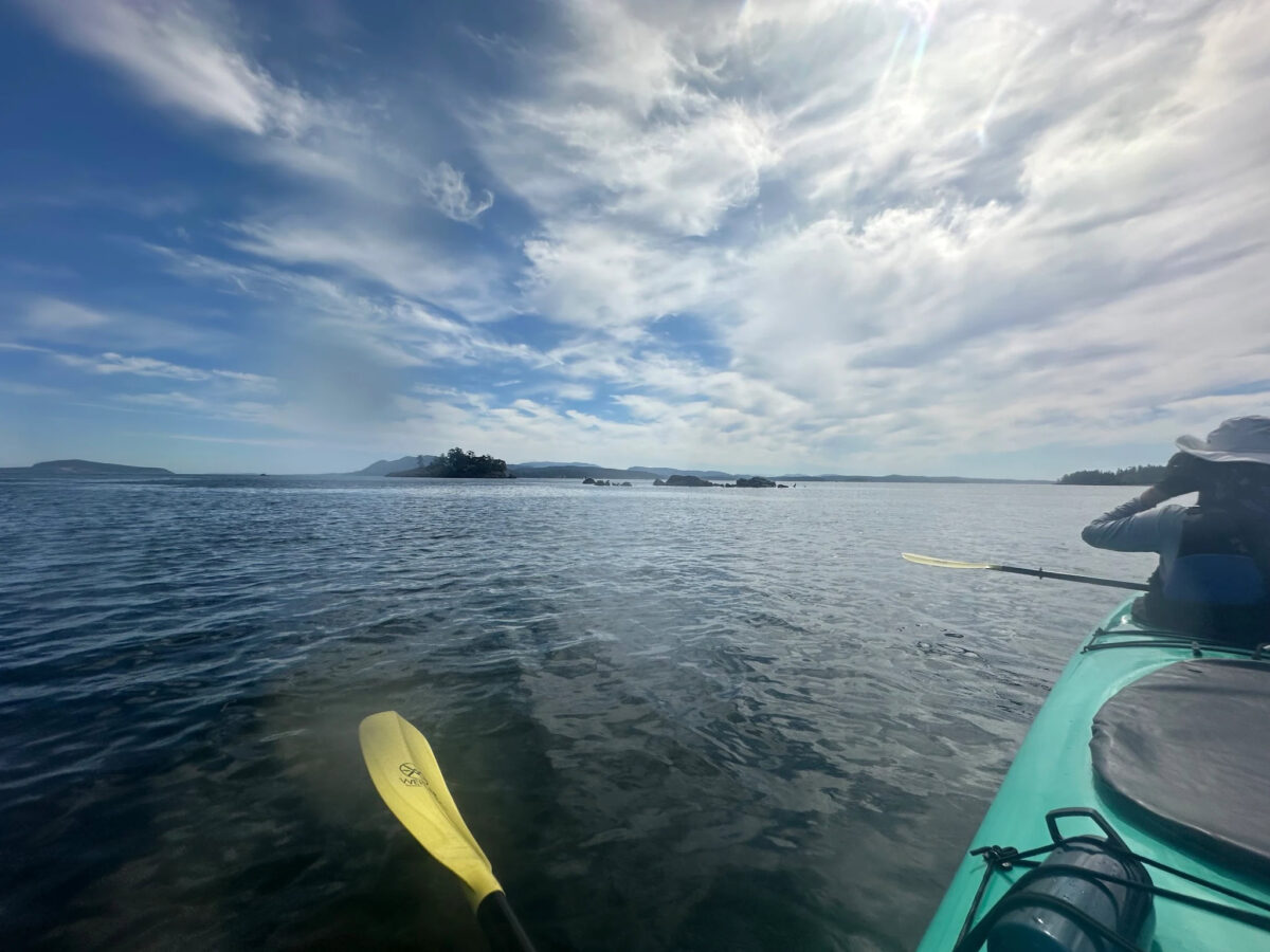 A person enjoys kayaking Seattle on a calm lake under a partly cloudy sky, with islands visible in the distance.