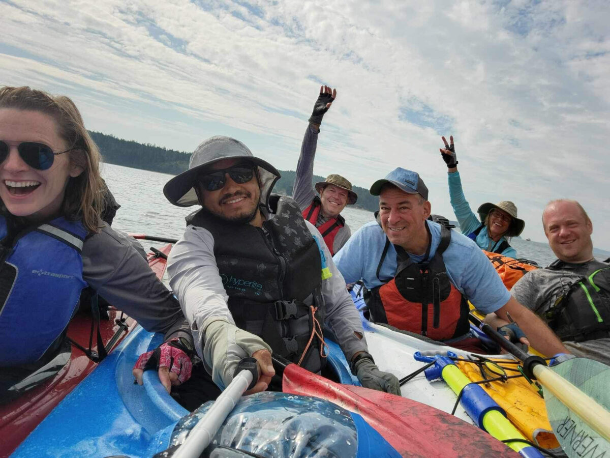 A group of six people in kayaks smile and pose for a selfie on the water under a partly cloudy sky, enjoying one of the popular Kayaking Tours in Seattle.