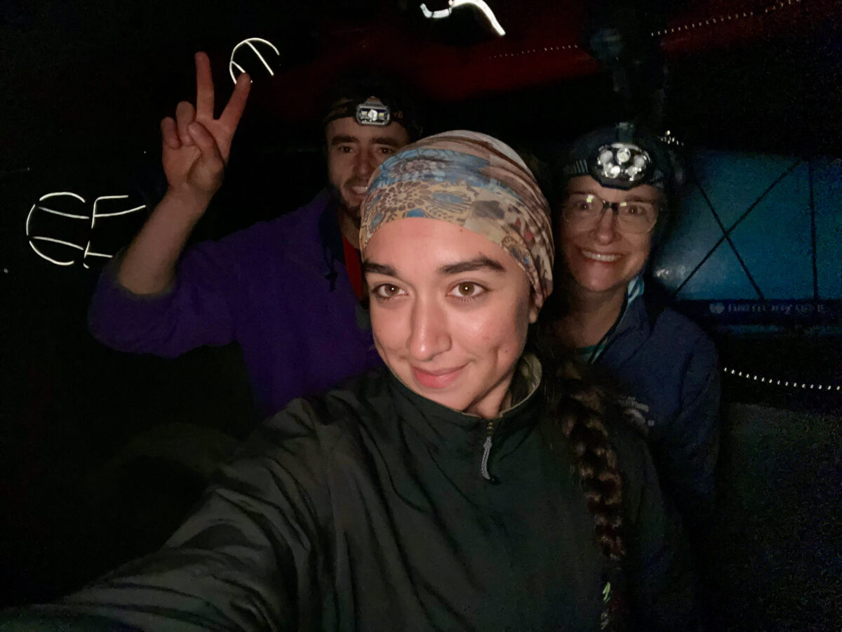 Three people wearing headlamps pose for a selfie in a dark setting after Friday Harbor kayaking. One person in the back flashes a peace sign, while the lighting highlights their smiling faces.