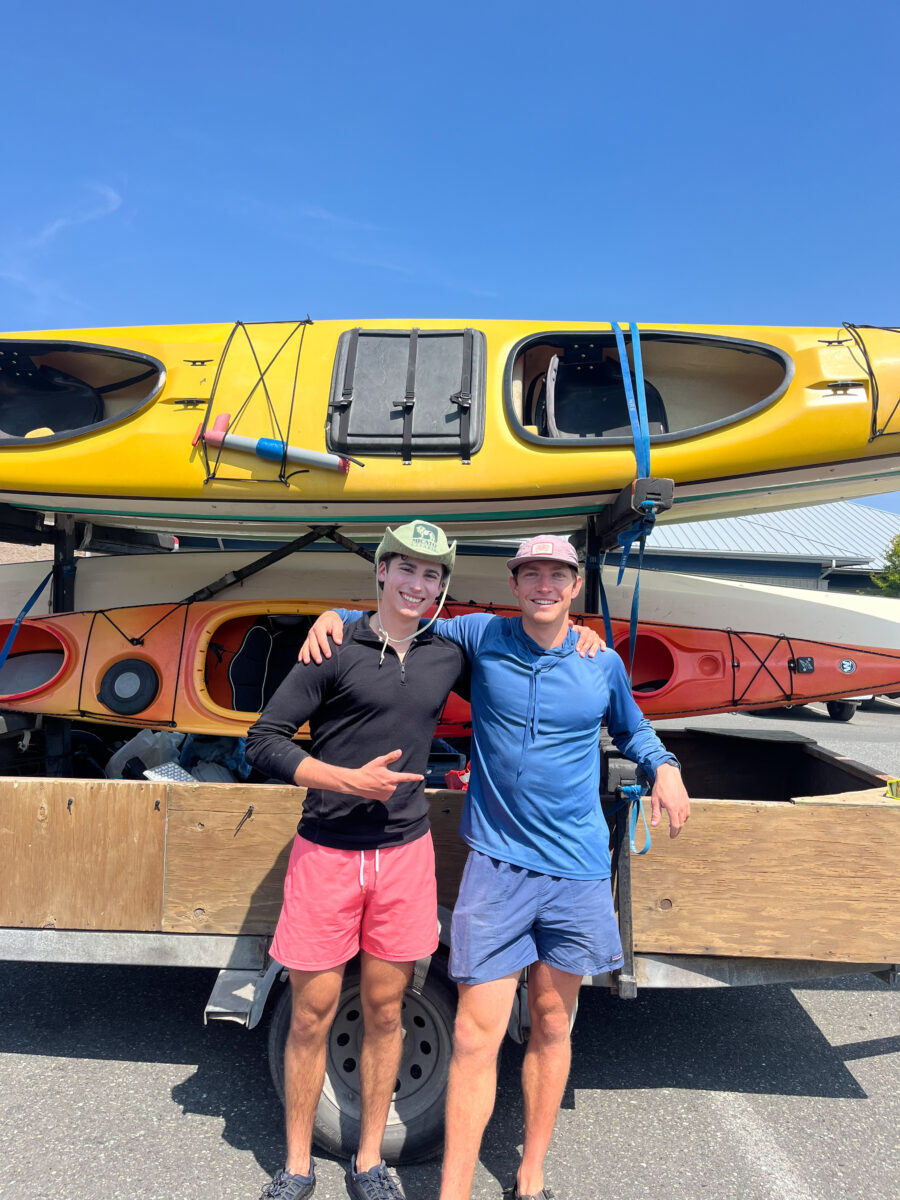 Washington Kayaking Guide to the Best Places, Wildlife, and Guided Tours 3 Two men in casual outdoor clothing stand smiling in front of a trailer loaded with kayaks, ready for a Washington Kayaking adventure on a sunny day.